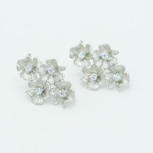 May include: A pair of silver-toned stud earrings, each featuring a cluster of four textured flower-shaped petals. Each individual flower petal has a small, clear, round-cut gemstone set in the center, creating a floral arrangement design.