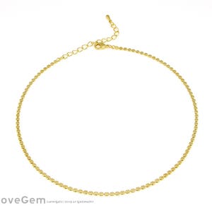 Puede incluir: Un collar de cadena de oro con un diseño delicado de cuentas. La cadena está hecha de pequeñas cuentas redondas que están espaciadas uniformemente.