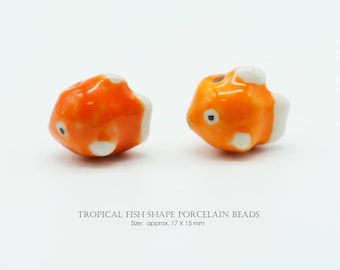 May include: Two orange porcelain beads shaped like tropical fish with white accents. The beads are approximately 0.67 x 0.59 inches in size. The text on the image reads "TROPICAL FISH SHAPE PORCELAIN BEADS".