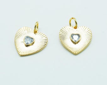 May include: Two gold-colored heart-shaped pendants with a textured, sunburst design. Each pendant features a small, clear heart-shaped stone in the center and a loop at the top for hanging. Jewelry.