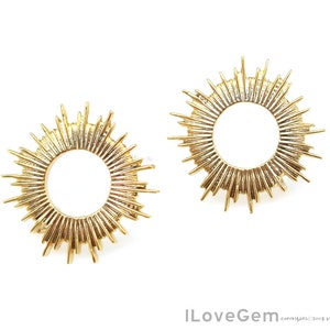 K&ouml;nnte beinhalten: Ein Paar goldene Sonnenstrahlen-Ohrringe mit einem runden Design. Die Ohrringe sind aus Metall und haben eine gl&auml;nzende Oberfl&auml;che.