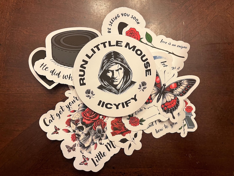 May include: A collection of stickers featuring various designs, including a skull with roses, a butterfly, a hooded figure with the text "Run Little Mouse Iicyify", and the text "He did what?", "Cat got your", "Love is an enigma", "Let ys it", "Lade", "and I bow to you", and "Little M".