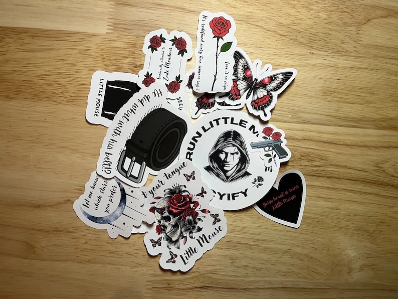May include: A collection of stickers featuring various designs, including a skull with flowers, a belt buckle, a butterfly, a gun, a moon, and a person with a hood. The stickers are printed on white paper with black ink and have red accents.