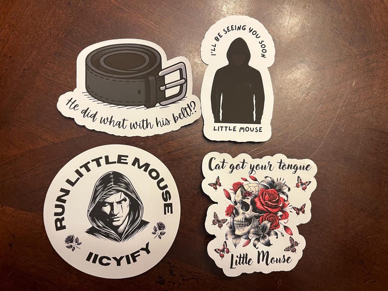 May include: Four stickers with black and white illustrations and text. The first sticker features a black leather belt with the text "He did what with his belt!?". The second sticker features a hooded figure with the text "I'll be seeing you soon" and "Little Mouse". The third sticker features a hooded figure with the text "Run Little Mouse Icyify". The fourth sticker features a skull with flowers and the text "Cat got your tongue" and "Little Mouse".