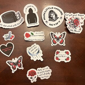May include: A set of ten stickers featuring various designs, including butterflies, flowers, hearts, and text. The stickers are printed on white paper with black outlines and red accents.
