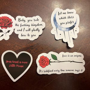 May include: Five stickers with different designs and text. One sticker features a red rose with the text "Baby, you rule the fucking kingdom, and I will gladly bow to you". Another sticker features a black heart with the text "Your heart is mine Little Mouse". A third sticker features a blue crescent moon with stars and the text "Let me know which stars you prefer". A fourth sticker features a red rose with a stem and the text "Love is an enigma. It's redefined every time someone says it". The fifth sticker features a red rose with a stem and the text "Love is an enigma. It's redefined every time someone says it".