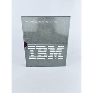 May include: A gray box with the IBM logo in white, and the text "Personal Computer Hardware Reference Library" at the top. The box has a textured surface and a dark red circle on the side.