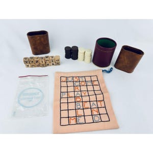 May include: A Scrabble game set with wooden letter tiles, brown and white game pieces, and three brown leather tile holders. A peach-colored fabric bag displays the words "JUST COME PLAY BEAT ME". A clear plastic bag is also included.