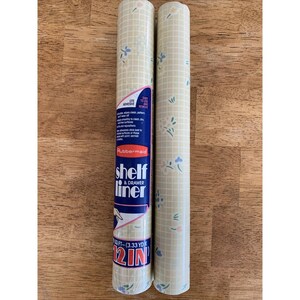 May include: Two rolls of shelf and drawer liner. The rolls are beige with a grid pattern and small blue and white floral designs. The label reads "shelf & drawer liner" and "12 IN".