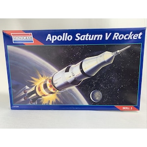 May include: A model kit box for the Apollo Saturn V Rocket. The box features a detailed illustration of the rocket in space, with the text "Apollo Saturn V Rocket" and the Monogram logo. The box is blue with a white rocket.