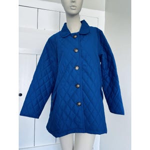 May include: A vibrant blue quilted jacket with a diamond pattern. The jacket features a classic collar, four brown buttons, and long sleeves. The jacket is displayed on a mannequin.