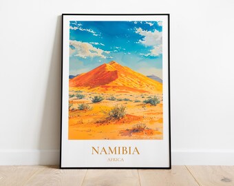 May include: A framed poster with a landscape image of a large orange sand dune in Namibia, Africa. The sky is blue with white clouds. The text "NAMIBIA" and "AFRICA" is printed in gold at the bottom of the poster.