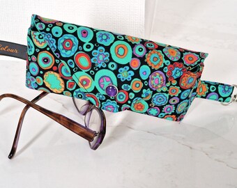 May include: A black eyeglass case with a colorful, abstract pattern of circles and flowers. The case has a snap closure and a strap with a metal clip.