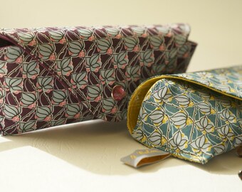 May include: Two patterned eyeglass cases, one in a purple and pink floral design and the other in a teal and yellow floral design. Both cases are made of fabric and have a soft, velvety lining.