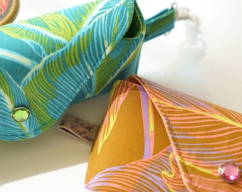 May include: Two fabric pouches with a tropical leaf pattern. The pouch on the left is teal and green with a green rhinestone. The pouch on the right is brown, pink, and purple with a pink rhinestone. Both pouches have a small brown tag that says "Lost Colour".