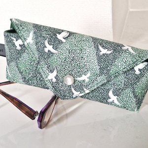 May include: A green and white patterned glasses case with a white bird design. The case has a flap closure and a small metal loop.