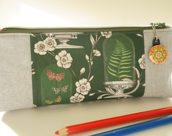 May include: A green and white zippered pencil case with a floral and butterfly design. The case has a gray fabric border and a small button with a colorful design.