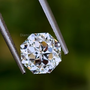 Pu&ograve; includere: Un diamante trasparente e sfaccettato tenuto da una pinza su uno sfondo verde. Il diamante ha un motivo a forma di stella.