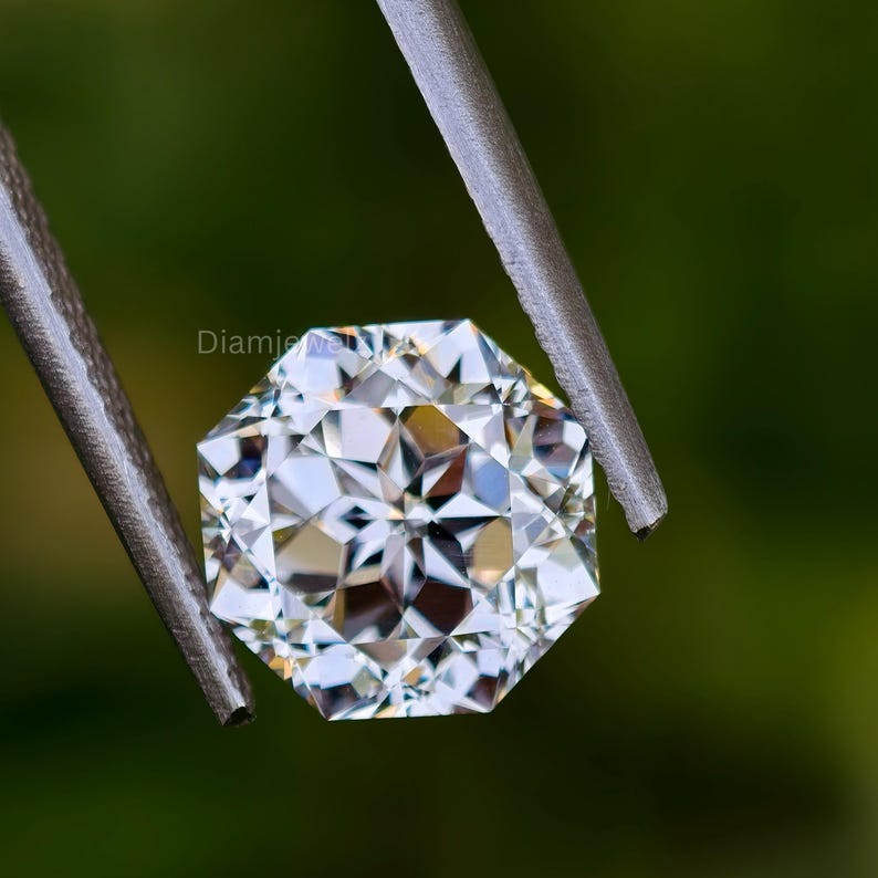 Pu&ograve; includere: Un diamante trasparente e sfaccettato tenuto da una pinza su uno sfondo verde. Il diamante ha un motivo a forma di stella.