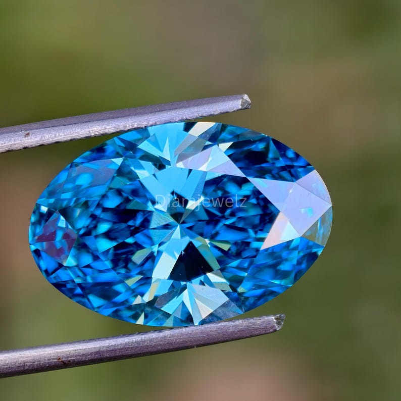 May include: A vibrant blue oval-shaped gemstone with a faceted cut, held by tweezers against a green background.