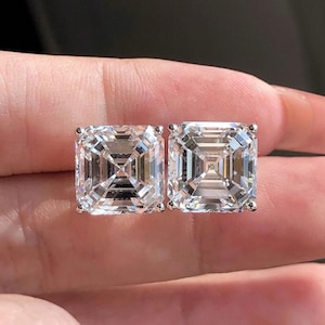 May include: A pair of square-shaped diamond earrings with a clear, faceted design. The earrings are set in a silver metal setting.