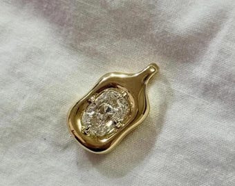May include: A gold pendant featuring a clear, oval-cut gemstone. The pendant has an irregular, flowing shape with a small loop at the top. The gemstone is set within the gold, creating a contrast. The pendant is likely for a necklace.