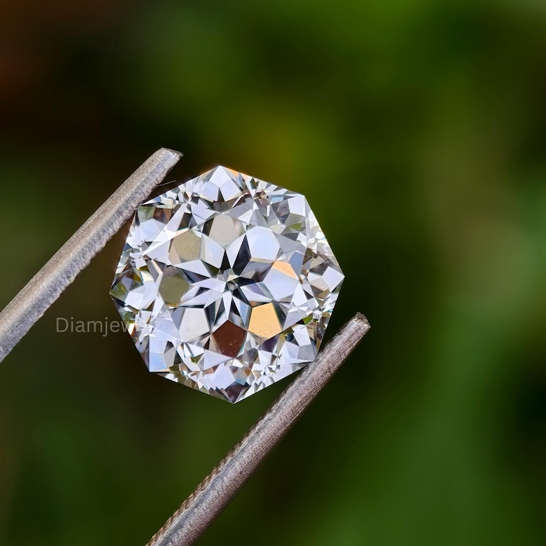 Pu&ograve; includere: Una gemma di diamante ottagonale, trasparente e sfaccettata, tenuta in una pinza di metallo su uno sfondo verde.