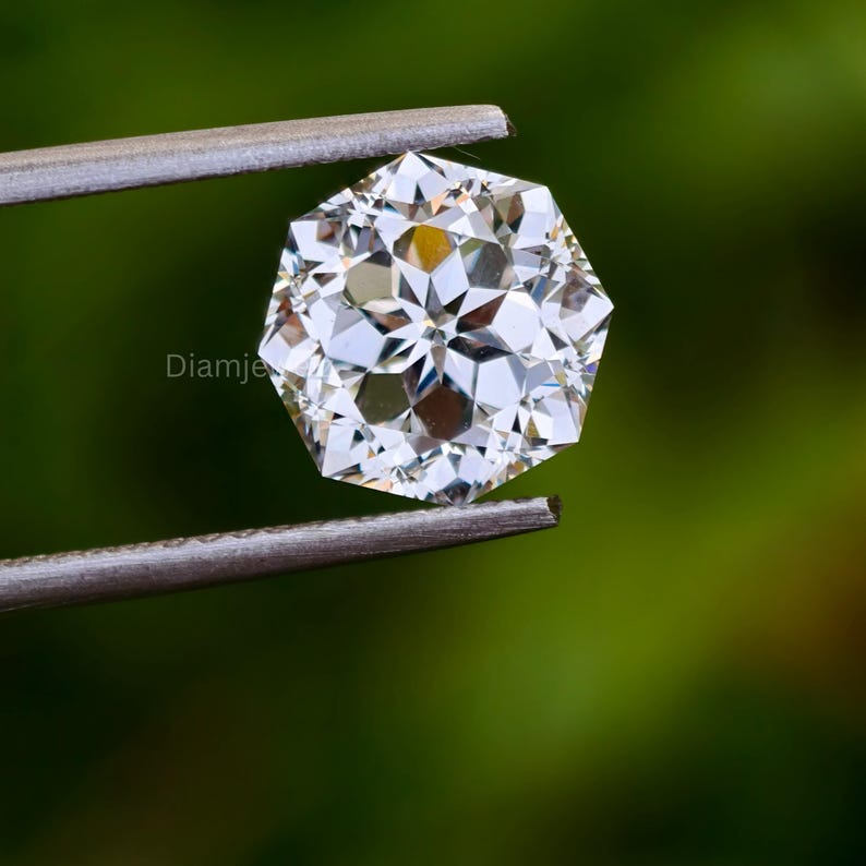 Pu&ograve; includere: Una gemma di diamante trasparente di forma ottagonale tenuta in pinzette su uno sfondo verde.