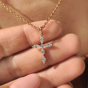 Può includere: Una collana a catena dorata con un ciondolo a croce. La croce è composta da cinque pietre trasparenti taglio marquise disposte in un motivo verticale e orizzontale, con una pietra rotonda trasparente incastonata al centro dell'incrocio.