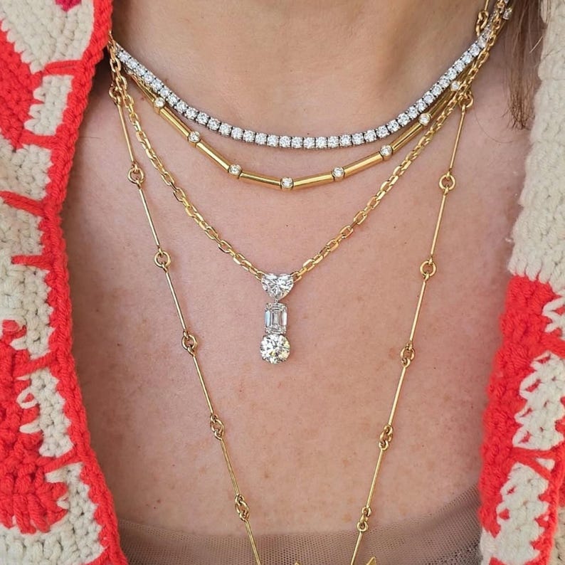 May include: A multi-layered necklace set with gold chains and diamond embellishments. The top layer is a diamond tennis necklace, followed by a gold chain with diamond details, and a gold chain with a diamond pendant. The longest chain has a delicate design.