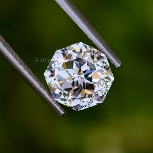 Pu&ograve; includere: Una gemma di diamante ottagonale, trasparente e sfaccettata, tenuta da una pinza su uno sfondo verde. Il diamante &egrave; tagliato con molte sfaccettature, creando un effetto scintillante.