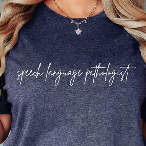 May include: A heather navy blue t-shirt with the text "speech language pathologist" written in white cursive script.