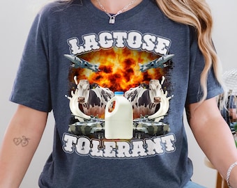 May include: Navy blue t-shirt with a graphic design featuring the text "LACTOSE TOLERANT". The design includes a milk jug, cows, jets, and an explosion. The shirt is a casual wear item.