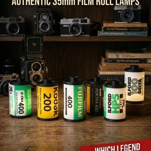 Peut inclure: Des lampes authentiques en forme de rouleaux de film 35mm, avec des marques comme Kodak, Fujifilm et Ilford. Elles sont présentées sur une étagère en bois avec des appareils photo anciens et des livres de photographie. Le texte dit "Explorez notre collection".