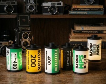 Peut inclure: Des lampes authentiques en forme de rouleaux de film 35mm, avec des marques comme Kodak, Fujifilm et Ilford. Elles sont présentées sur une étagère en bois avec des appareils photo anciens et des livres de photographie. Le texte dit "Explorez notre collection".