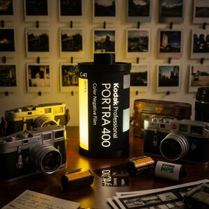 May include: A collection of vintage cameras, film rolls, and a Kodak PORTRA 400 film canister lamp. The scene includes a wall of framed photographs, creating a nostalgic atmosphere. The lamp is black with white text.
