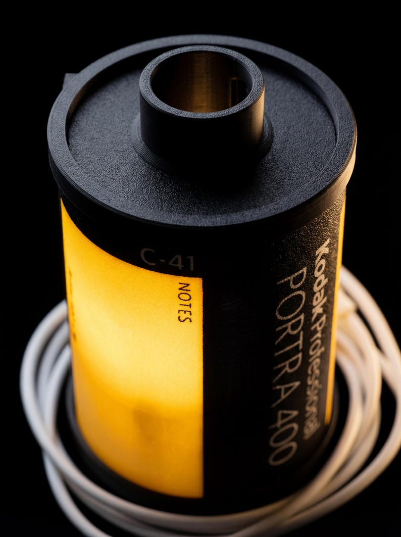 May include: A black and yellow Kodak Portra 400 film canister with white cord wrapped around it. The canister has the text "Kodak Professional PORTRA 400" and "NOTES" printed on it. The film is C-41.