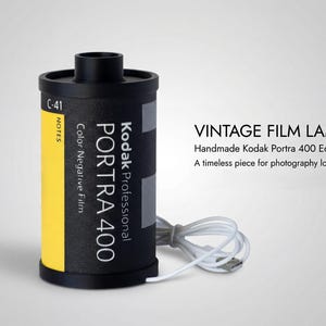 May include: A vintage film lamp crafted from a Kodak Portra 400 film canister. The black canister features a yellow stripe and white text. A white USB cable is attached. The image text reads "VINTAGE FILM LAMP".