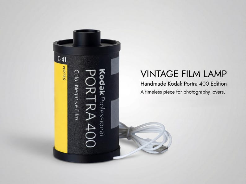 May include: A vintage film lamp crafted from a Kodak Portra 400 film canister. The black canister features a yellow stripe and white text. A white USB cable is attached. The image text reads "VINTAGE FILM LAMP".