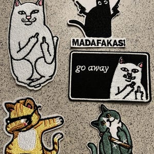 May include: A collection of embroidered patches featuring cartoon cats in various poses. One white cat gives the middle finger, while another black cat holds guns and the text reads "PEW PEW". Other patches include text that reads "MADAFAKAS!" and "go away".