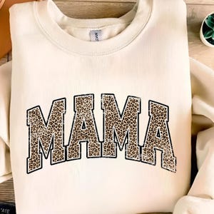 May include: A cream-colored sweatshirt with the word "MAMA" printed in black outlined letters. The letters are filled with a brown and black leopard print pattern.