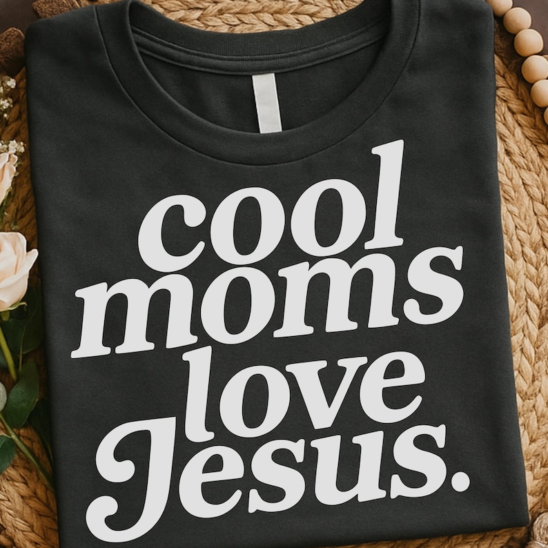 K&ouml;nnte beinhalten: Ein dunkelgraues T-Shirt mit dem Text "cool moms love Jesus" in gro&szlig;en, wei&szlig;en, fetten Buchstaben. Das T-Shirt mit Rundhalsausschnitt ist aus einem weichen Material gefertigt. Der Text ist mittig auf der Vorderseite des Kleidungsst&uuml;cks platziert.