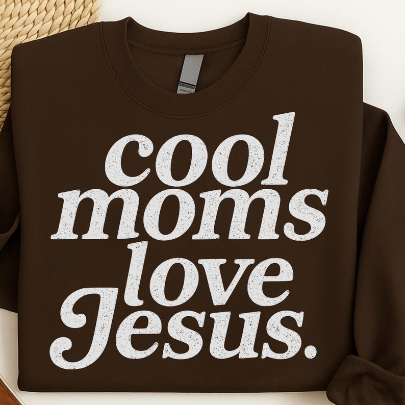 K&ouml;nnte beinhalten: Ein braunes Sweatshirt mit dem wei&szlig;en Text "cool moms love Jesus" in einer verwitterten Schriftart. Das Kleidungsst&uuml;ck hat einen Rundhalsausschnitt und lange &Auml;rmel. Der Text ist mittig auf der Vorderseite des Sweatshirts platziert.