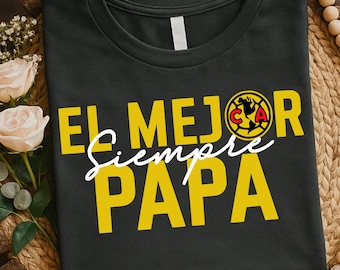 Può includere: T-shirt grigio scuro con testo giallo "EL MEJOR SIEMPRE PAPA" e un logo. Il testo è in grassetto, senza grazie, con "Siempre" in corsivo. Il logo è un emblema circolare con elementi rossi, gialli e neri.