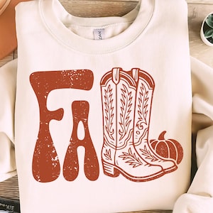 May include: Cream-colored sweatshirt with the word "FALL" in a distressed orange font. The design includes orange cowboy boots and a pumpkin, evoking an autumn theme.
