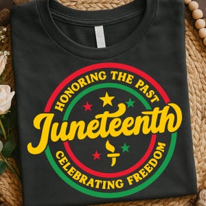 Peut inclure: T-shirt noir avec un motif circulaire célébrant le Juneteenth. Le motif comprend les mots "Honoring the Past" et "Celebrating Freedom" en cercle, avec "Juneteenth" en jaune. Le motif comporte également des étoiles et une torche.