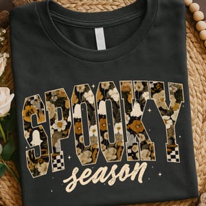May include: Dark gray t-shirt with the words "SPOOKY season" in a floral design. The letters are filled with a pattern of white, brown, and yellow flowers. The word "season" is in a cursive font.
