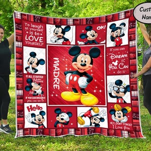 Puede incluir: Un edred&oacute;n rojo y blanco con el tema de Mickey Mouse con varias im&aacute;genes de Mickey Mouse y citas inspiradoras. El edred&oacute;n presenta una gran imagen central de Mickey Mouse y est&aacute; sostenido por dos personas en un entorno exterior cubierto de hierba.