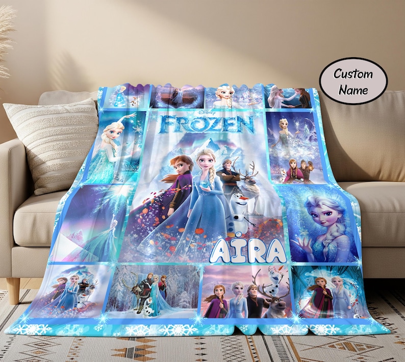 以下が含まれることがあります： エルサ、アナ、オラフをフィーチャーした、青と白のフローズンをテーマにしたブランケット。 ブランケットには「FROZEN」の文字と「AIRA」の名前がプリントされたコラージュデザインが施されています。 ブランケットはベージュのソファに掛けられています。