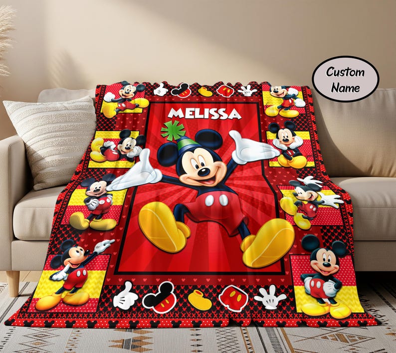 Puede incluir: Una manta roja, negra y amarilla con el tema de Mickey Mouse. La manta presenta una imagen grande de Mickey Mouse con el nombre "Melissa" y varias im&aacute;genes m&aacute;s peque&ntilde;as de Mickey Mouse. La manta est&aacute; sobre un sof&aacute; beige.